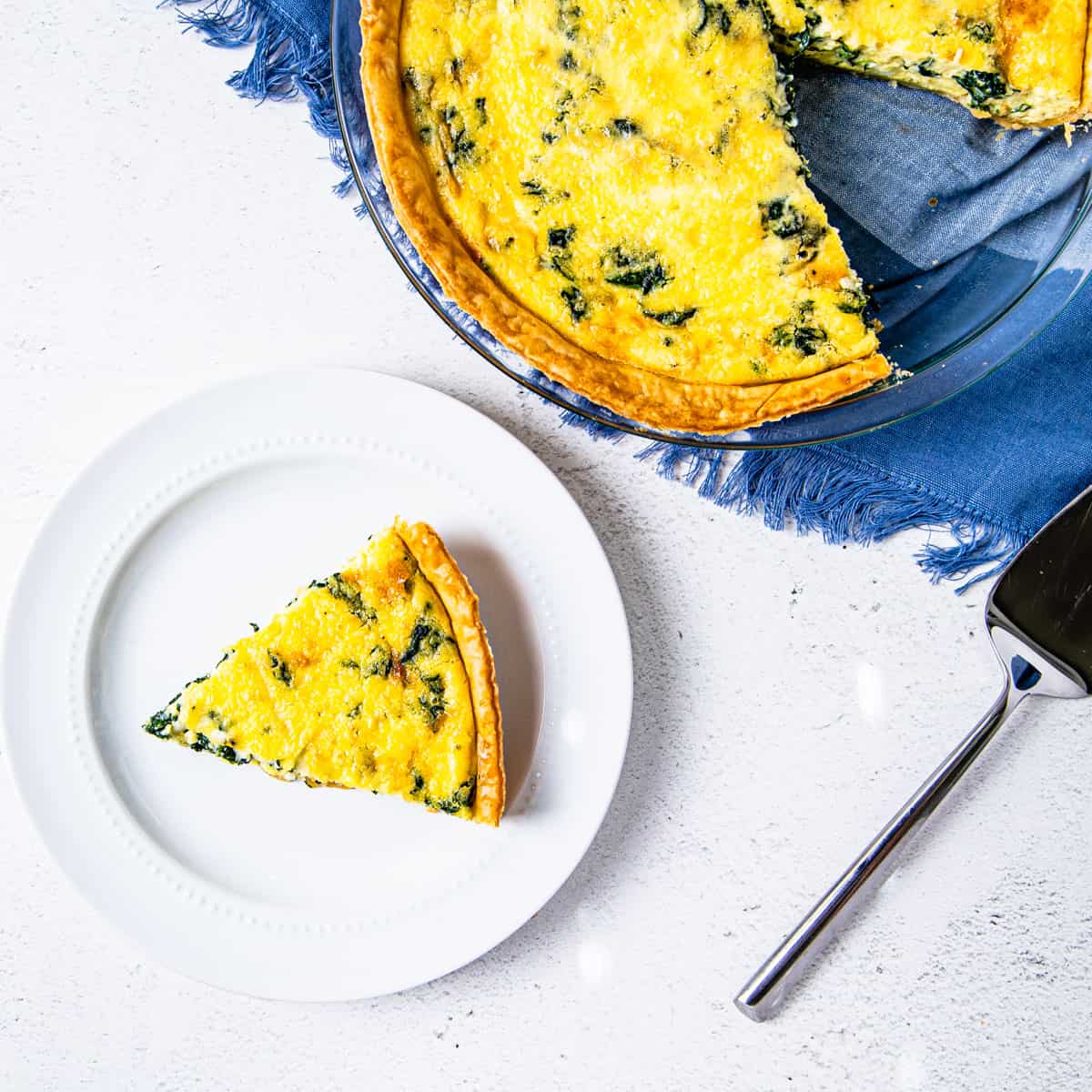 A pie dish of Quiche Florentine with a slice removed and served on a plate next to the dish. 