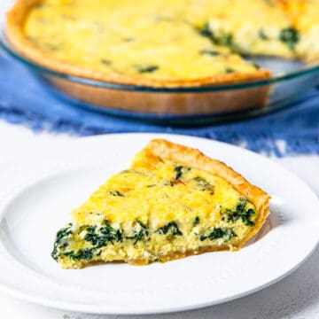 A slice of quiche florentine on a plate with a pie dish of Quiche Florentine in the background.