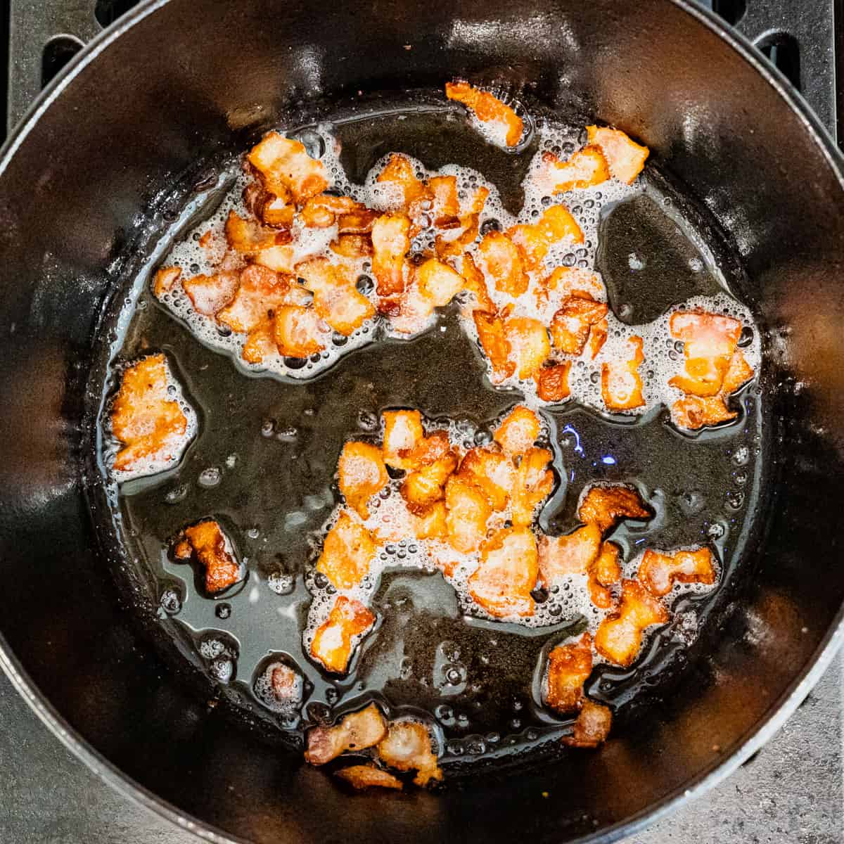 Strips of bacon being cooked in a cast iron pot.