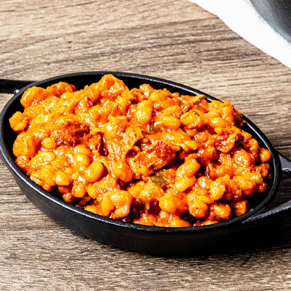 A small cast iron dish on a wooden table filled with smoked baked beans.