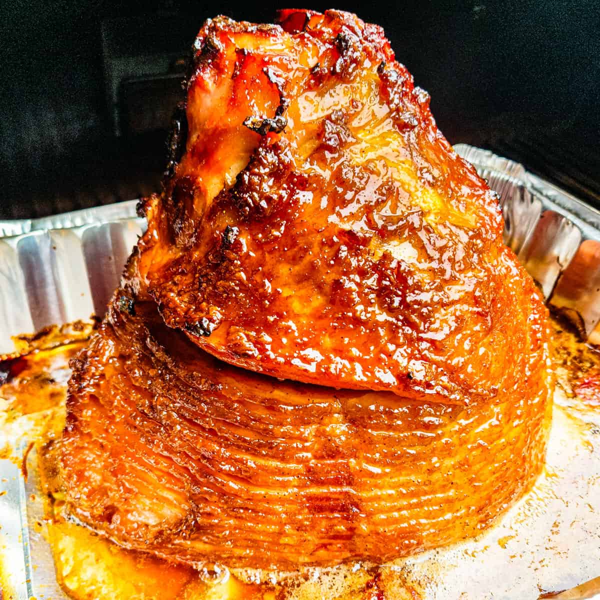 A spiral sliced ham coated with a honey brown sugar glaze cooking in a smoker.