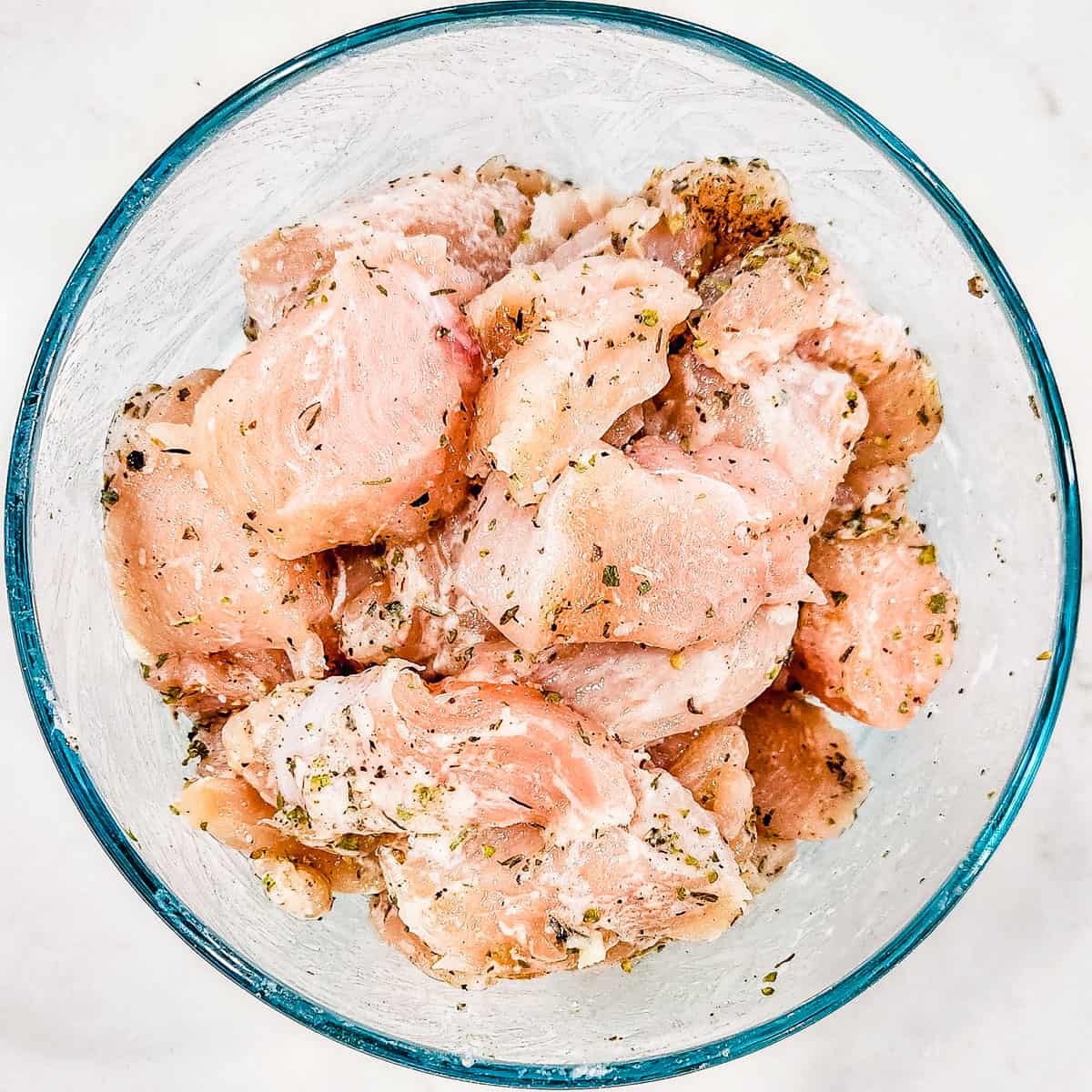 Chunks of chicken breast in a bowl tossed with flour and seasonings.