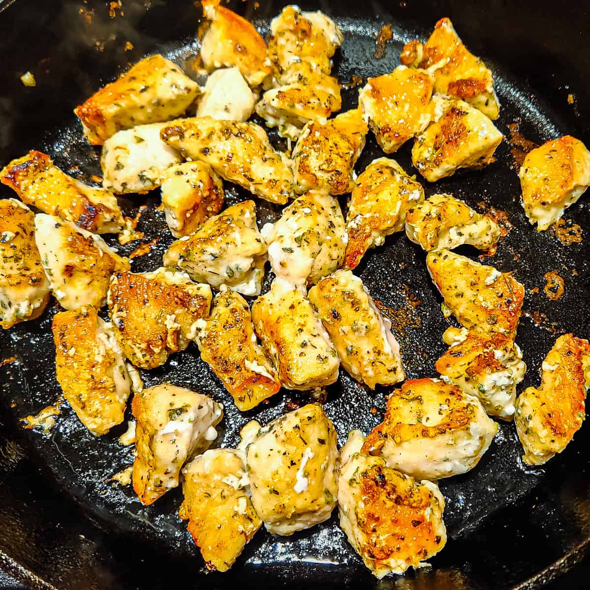 Chunks of chicken being cooked in a large skillet.