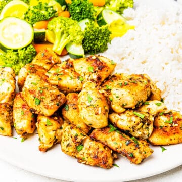 A plate of bite-sized chunks of chicken tossed in garlic butter served with vegetables and rice.