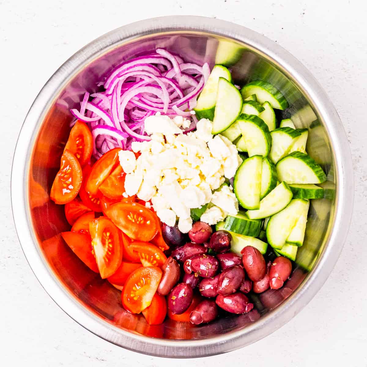 Greek salad ingredients in a mixing bowl before adding dressing and stirring to combine.
