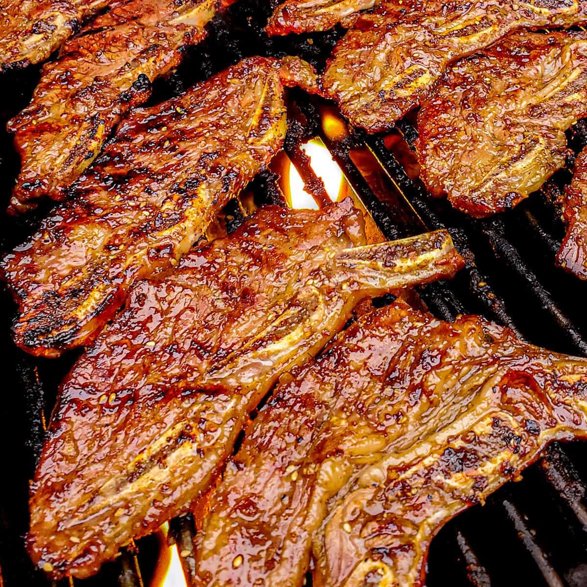 Korean marinated short ribs being cooked on a flaming grill.