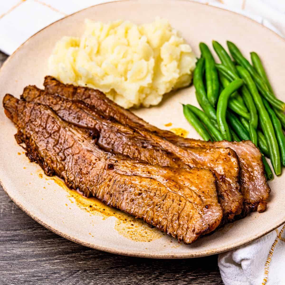 Sliced brisket served with mashed potatoes and green beans.