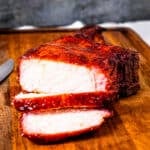 A smoked thick cut bone in pork chop with slices cut off on a cutting board.