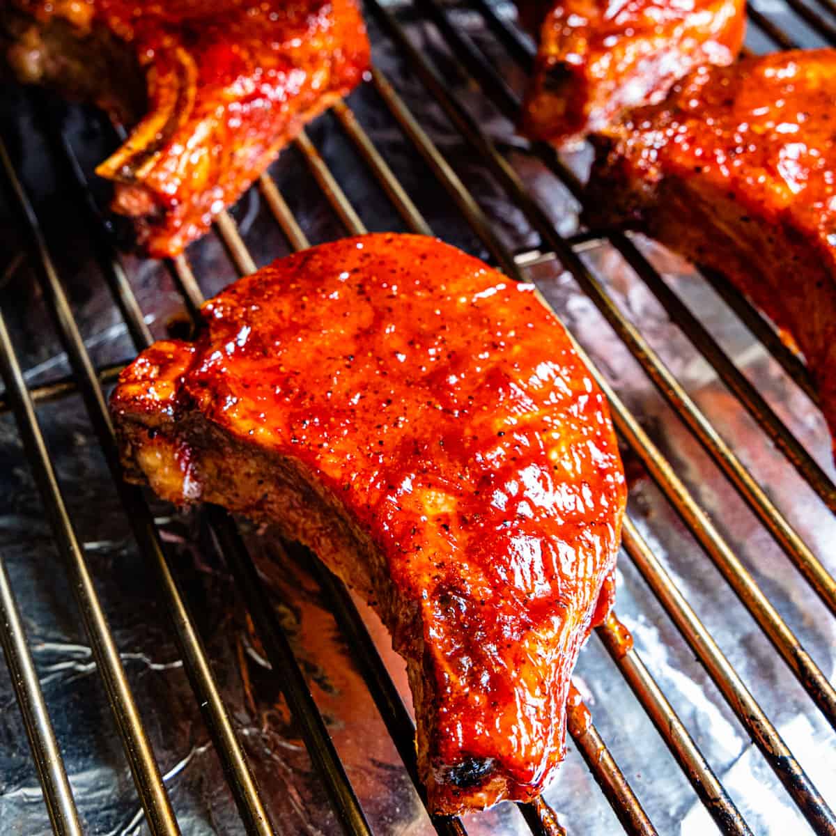 Pork chops on a grill coated with BBQ sauce.