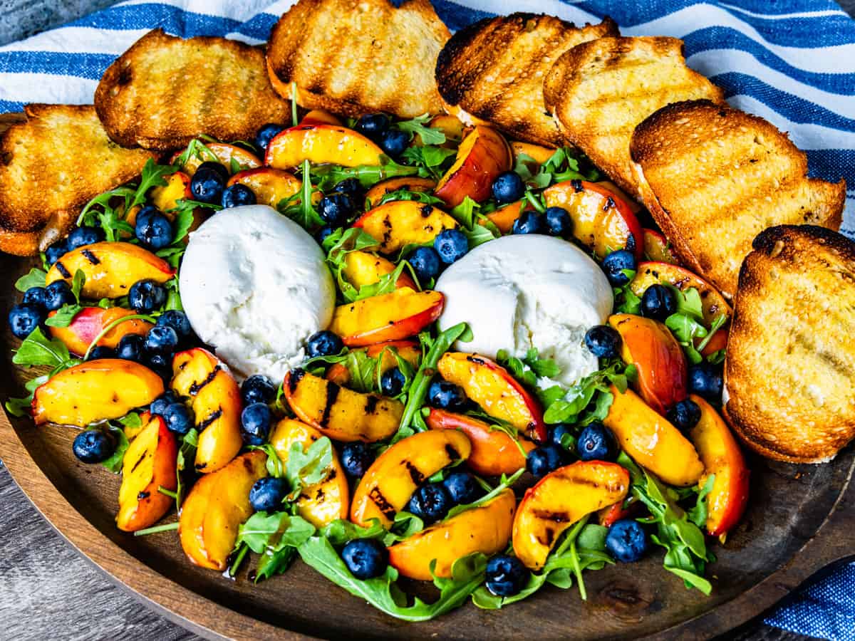 A salad with grilled peaches and burrata served on a large platter.