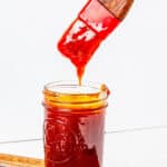 A basting brush being dipped into a jar of Peach BBQ sauce.