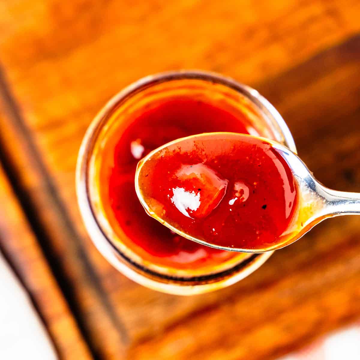 A spoonful of BBQ sauce held above a jar of the sauce.