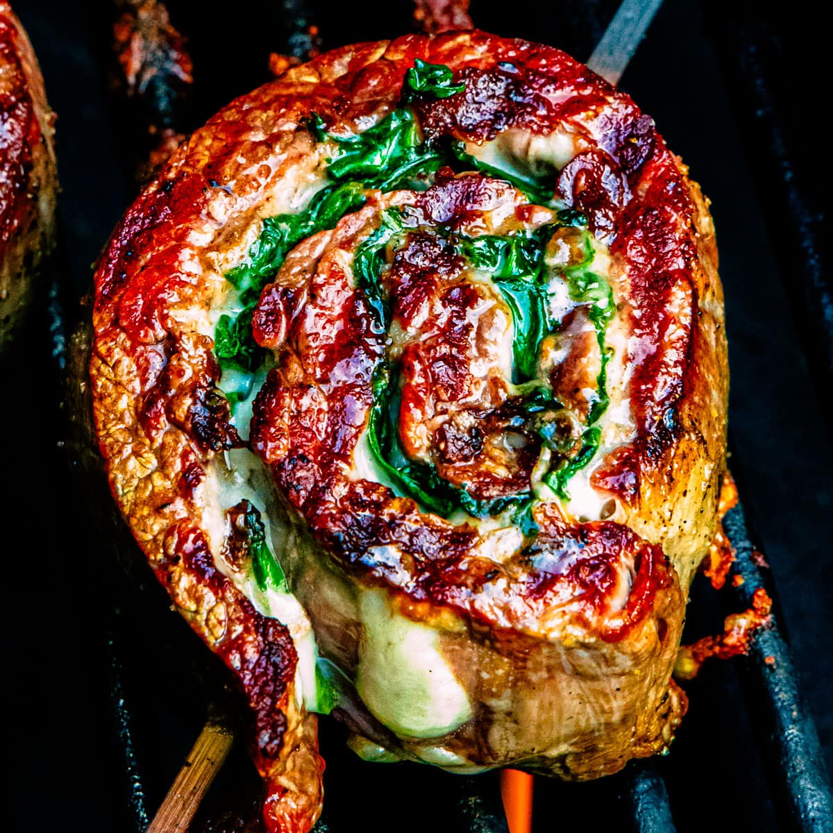 A flank steak pinwheel cooking on a grill.