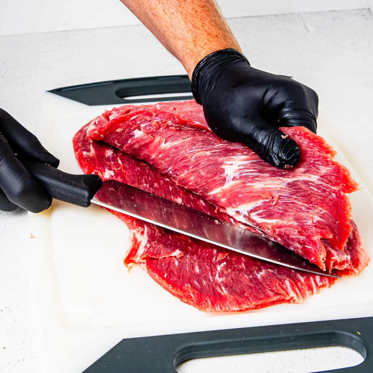 Flank steak being butterflied with the top portion being lifted up and sliced in the middle.