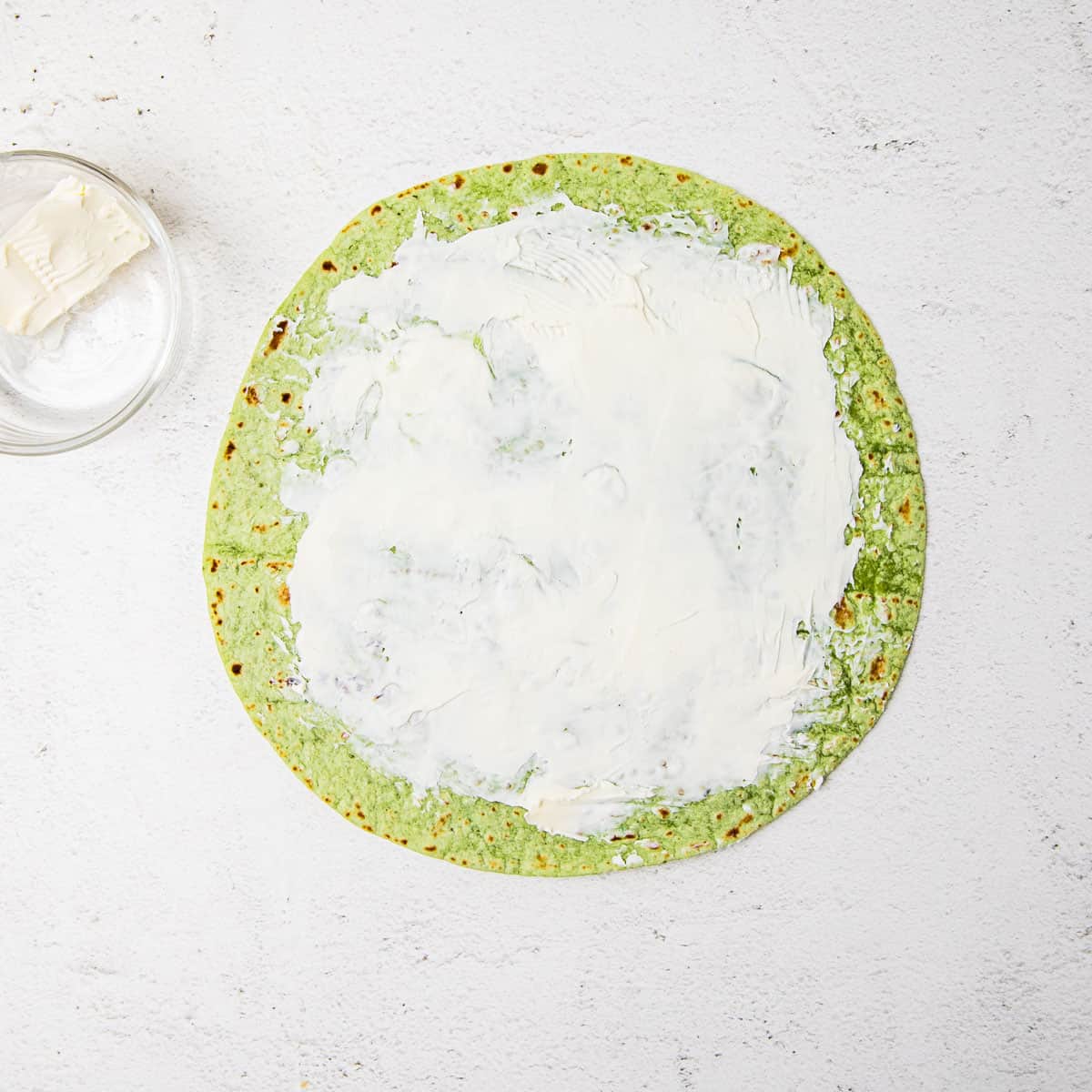 A tortilla on a countertop with a layer of cream cheese spread on top. 