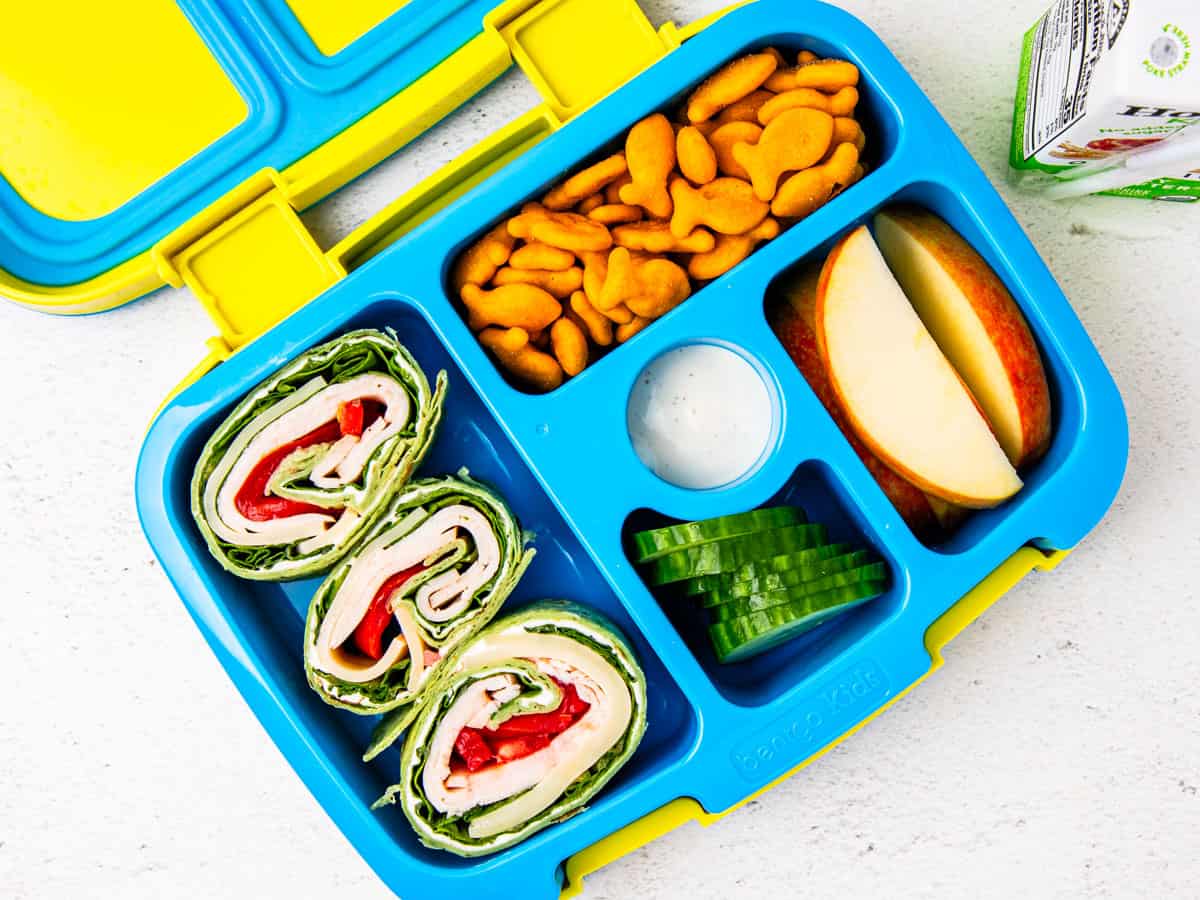 A bento box lunchbox with turkey pinwheels, apples, and Goldfish crackers.