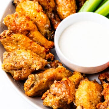 A plate of chicken wings served with ranch dressing and celery.