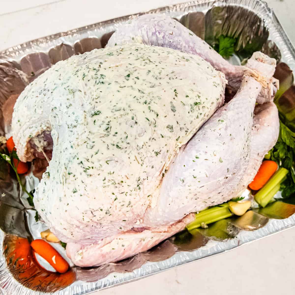 A whole turkey coated with herb butter and set in a roasting pan.