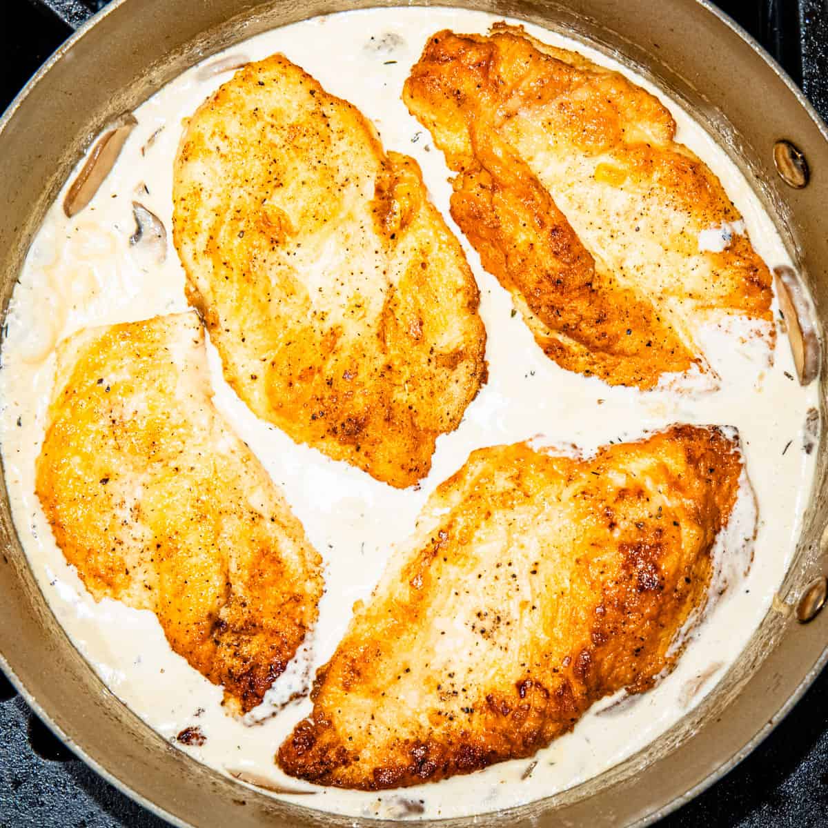 Chicken breasts in a mushroom cream sauce, cooking in a pan. 