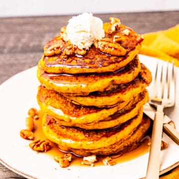 A large stack of pumpkin pancakes topped with butter, pecans, and syrup.