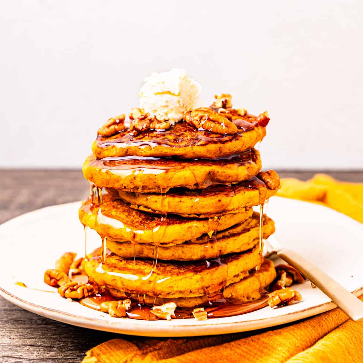 A stack of pumpkin pancakes topped with butter, pecans, and syrup.