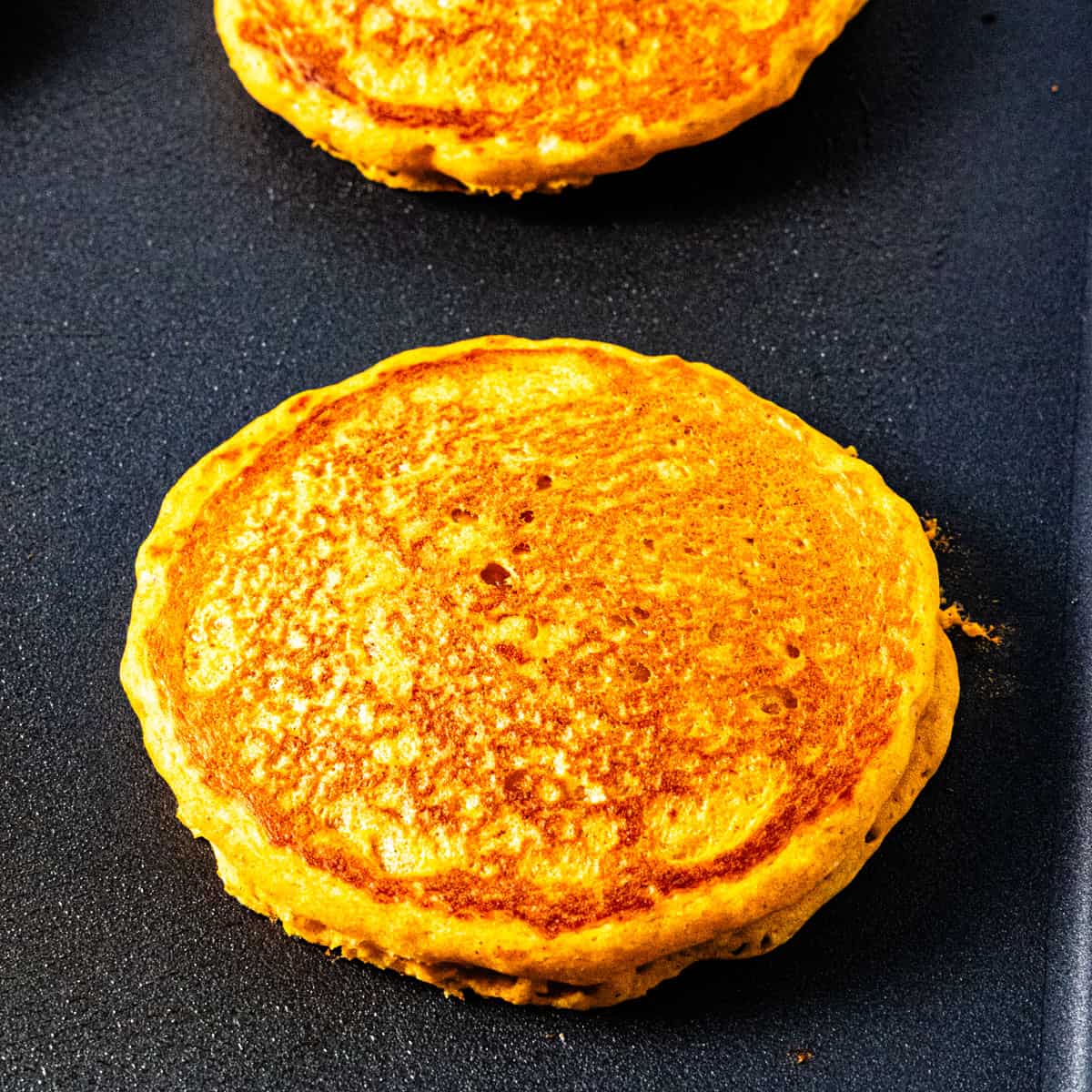 A cooked pumpkin pancake on a griddle. 