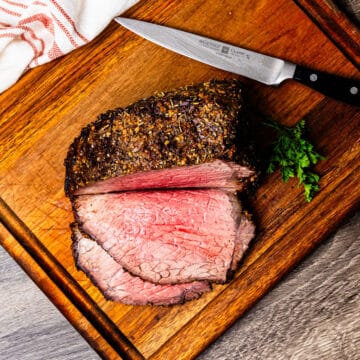 Bottom round roast beef being sliced on a cutting board.