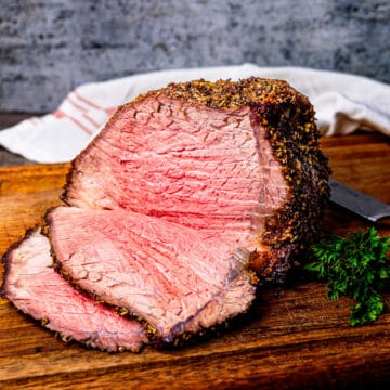 Bottom round roast beef being sliced on a cutting board.