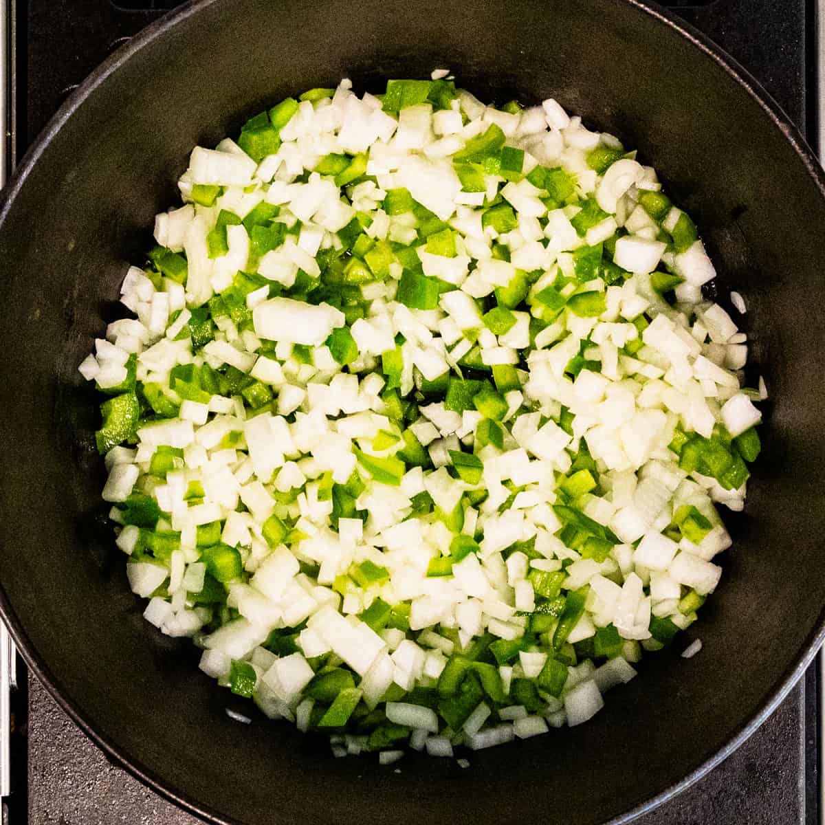 Chopped onion and green pepper cooking in a large pot.