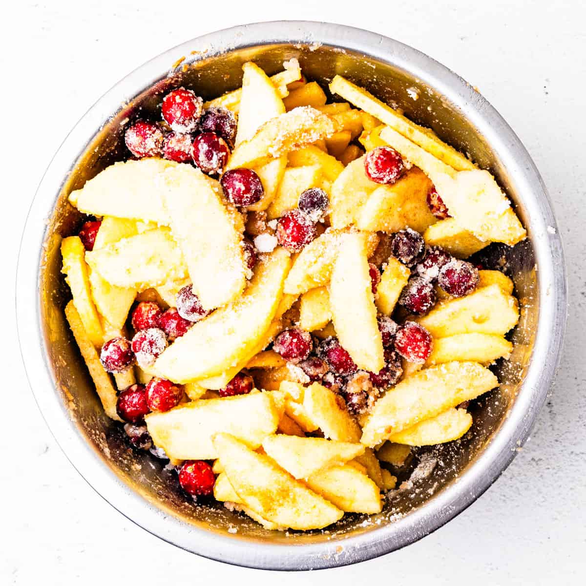 Cranberries and sliced apples in a mixing bowl mixed with sugar, flour, and cinnamon. 