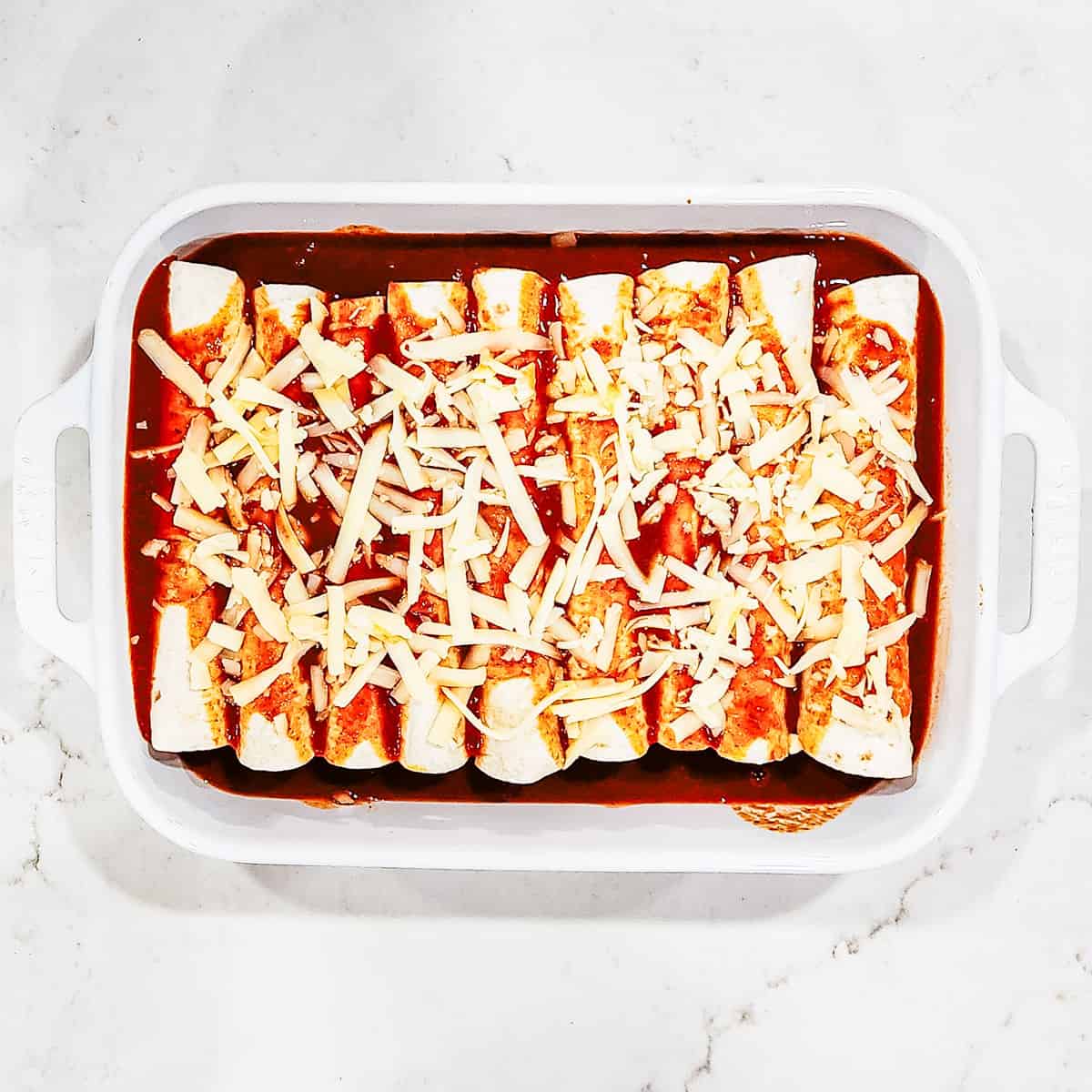 Enchiladas in a baking dish, covered in sauce and cheese, before being baked.