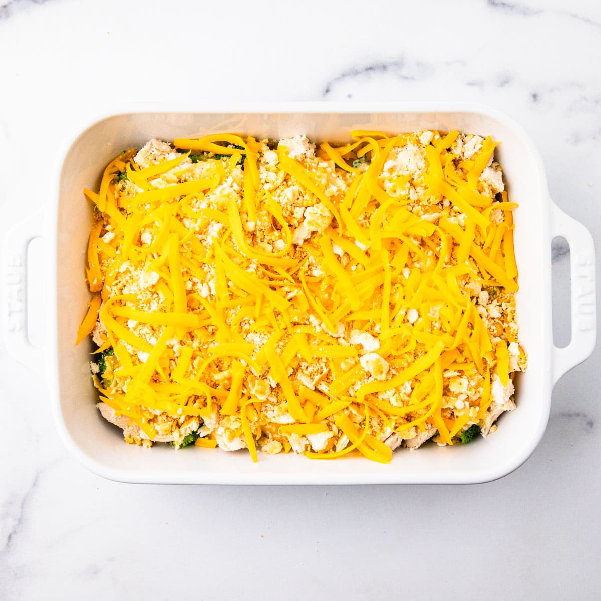 A casserole topped with cheese and crushed crackers before baking.