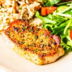 A seared pork chop on a plate with rice and a salad.
