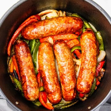 Cooked Italian sausages in an air fryer basket with peppers and onions.