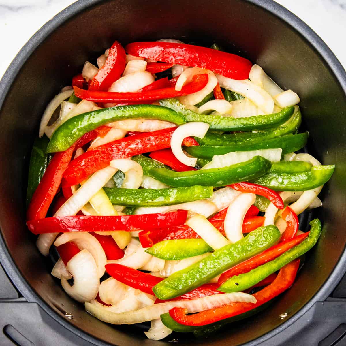 Peppers and onions in an air fryer basket.