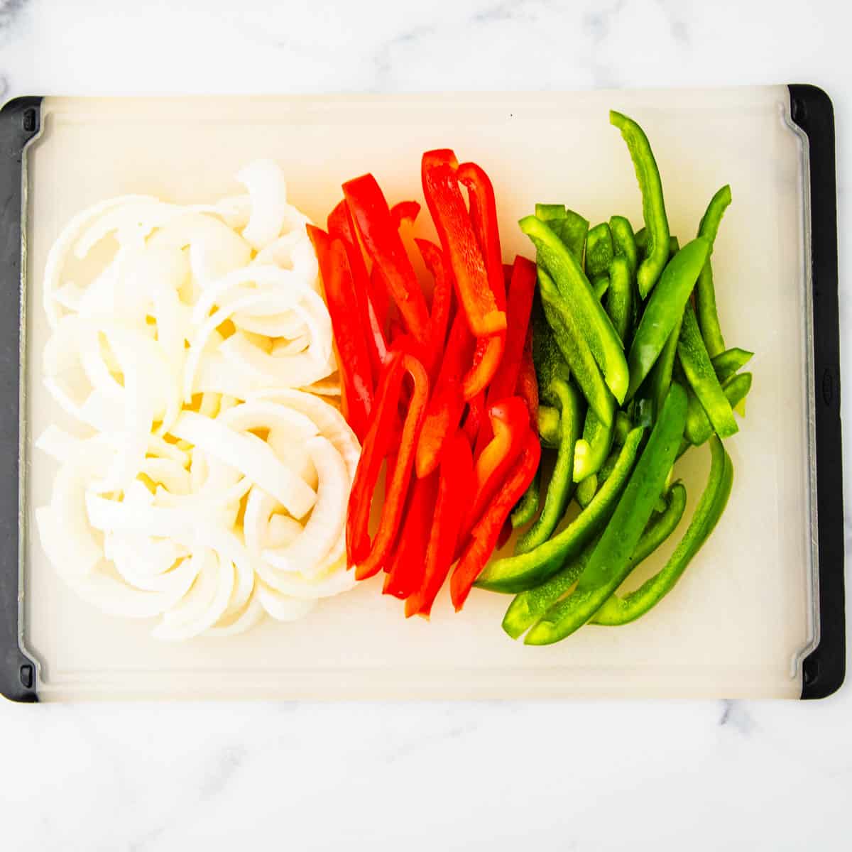Sliced peppers and onions on a cutting board.