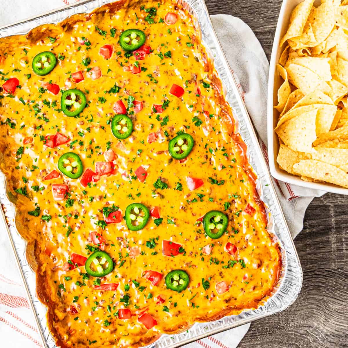 A pan of smoked queso dip on a table with a bowl of tortilla chips.