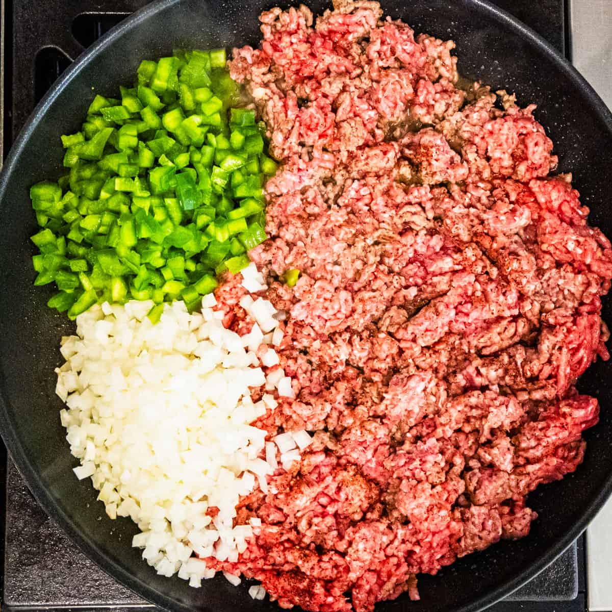 Ground beef in a large pan with diced green pepper and onion.