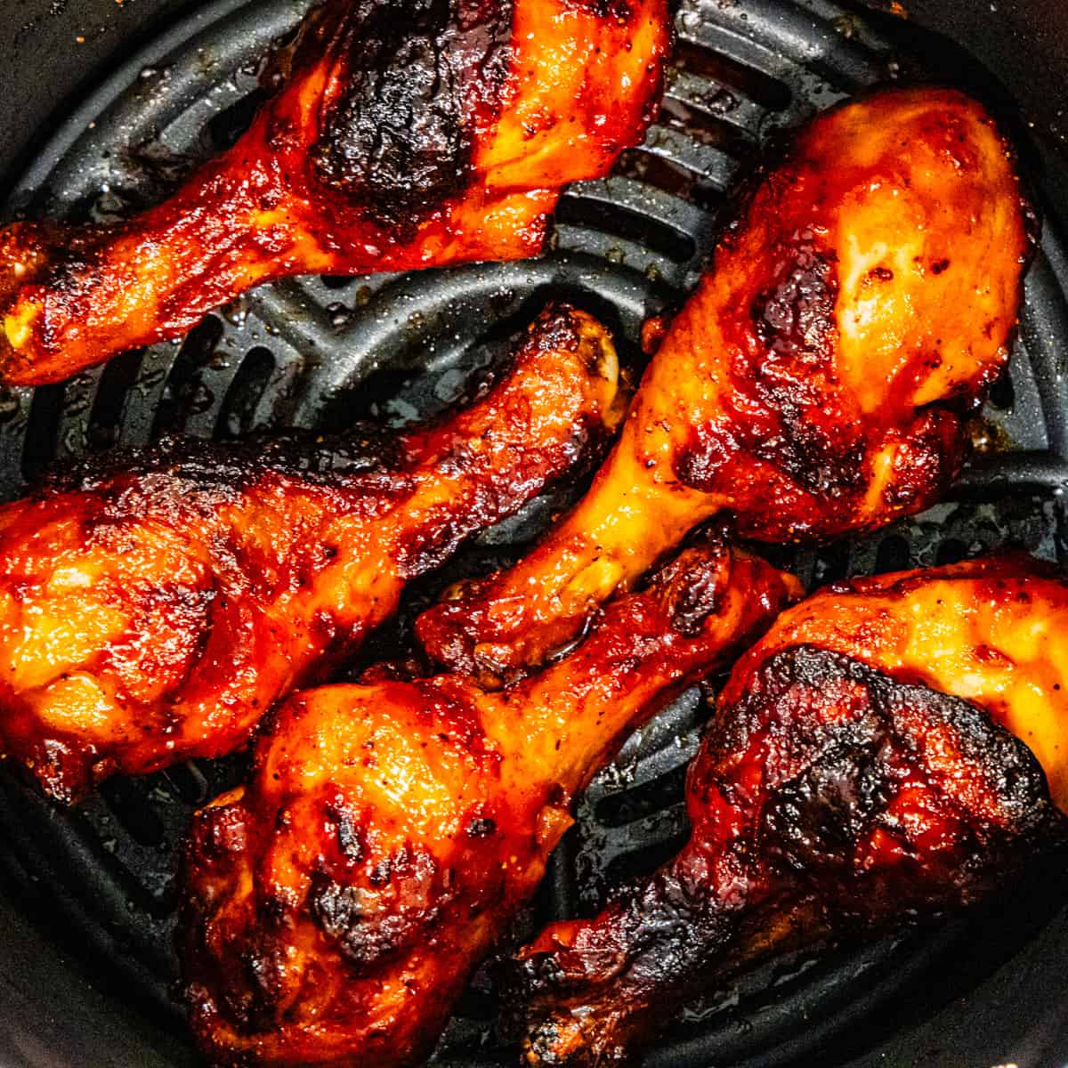 Cooked barbecue chicken legs in an air fryer basket.