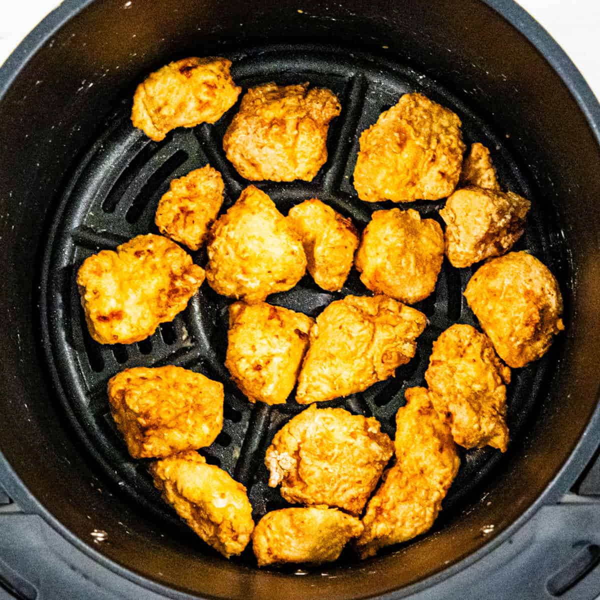 Cooked chicken bites in an air fryer basket.