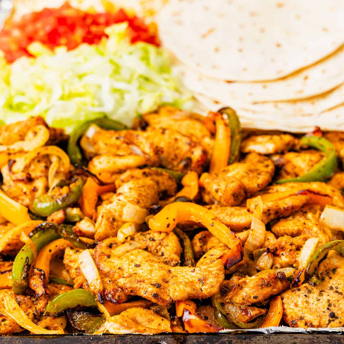 Chicken fajitas served with lettuce, tomato, cheese, and tortillas. 