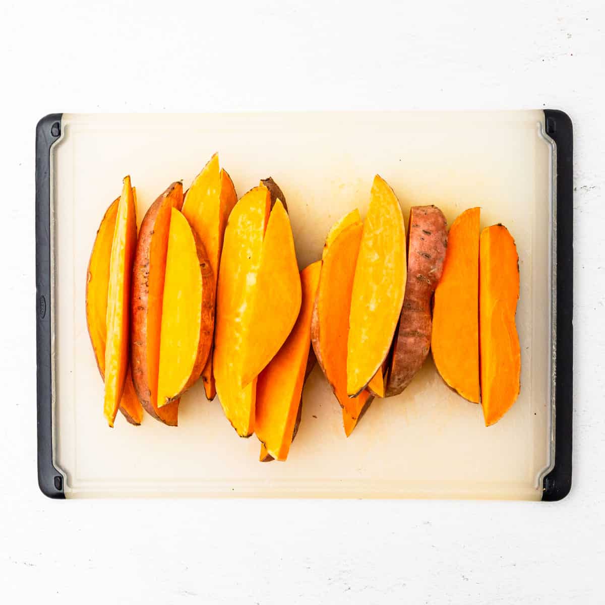 Sweet potatoes cut into wedges on a cutting board.