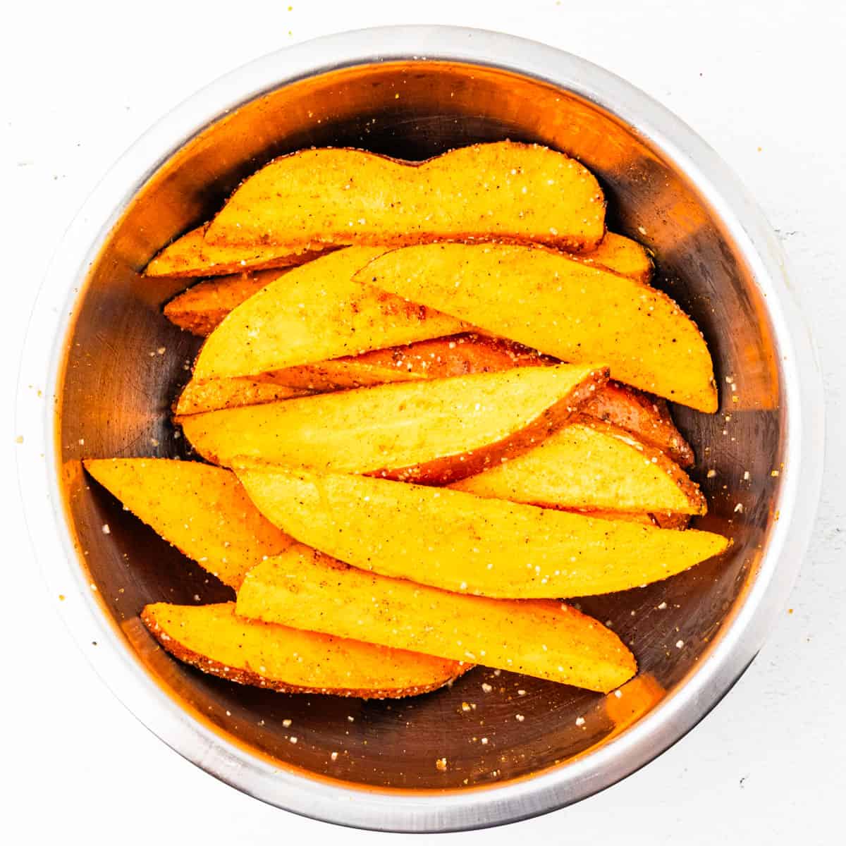 Sweet potatoes in a mixing bowl tossed with oil and seasonings.