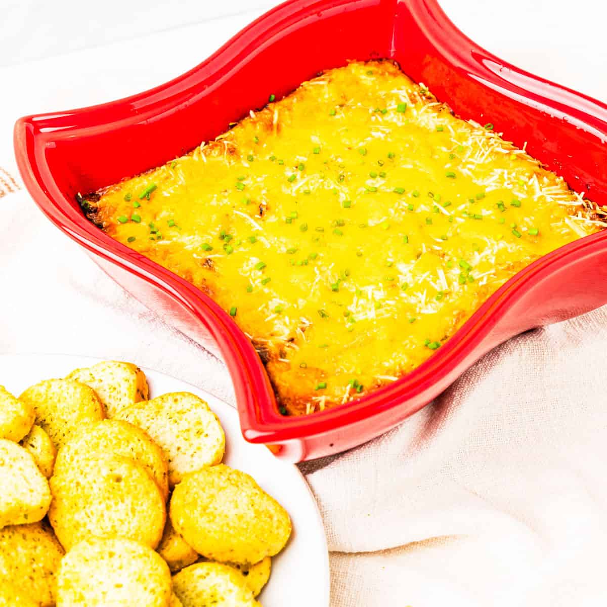 A baking dish of crab dip with a plate of crackers on a table.
