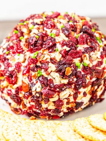 A cranberry and pecan crusted cheeseball served on a platter with crackers.