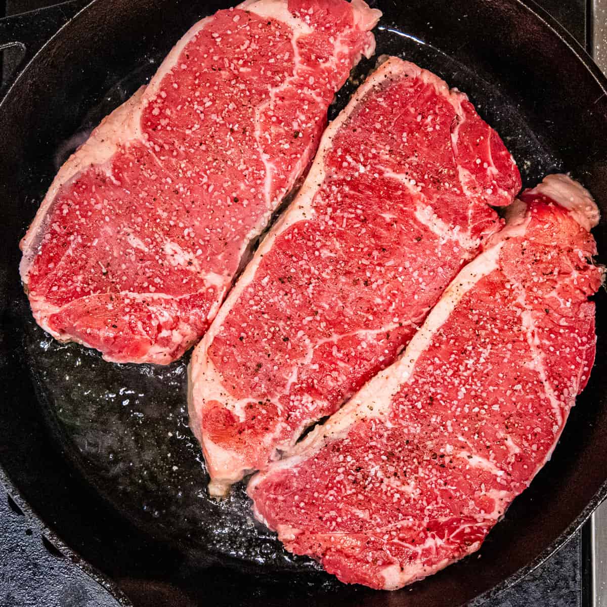 Steaks cooking in a cast iron pan.