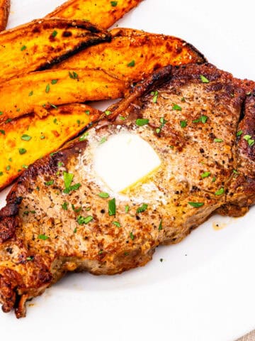 New York strip steak served on a plate with sweet potatoes.