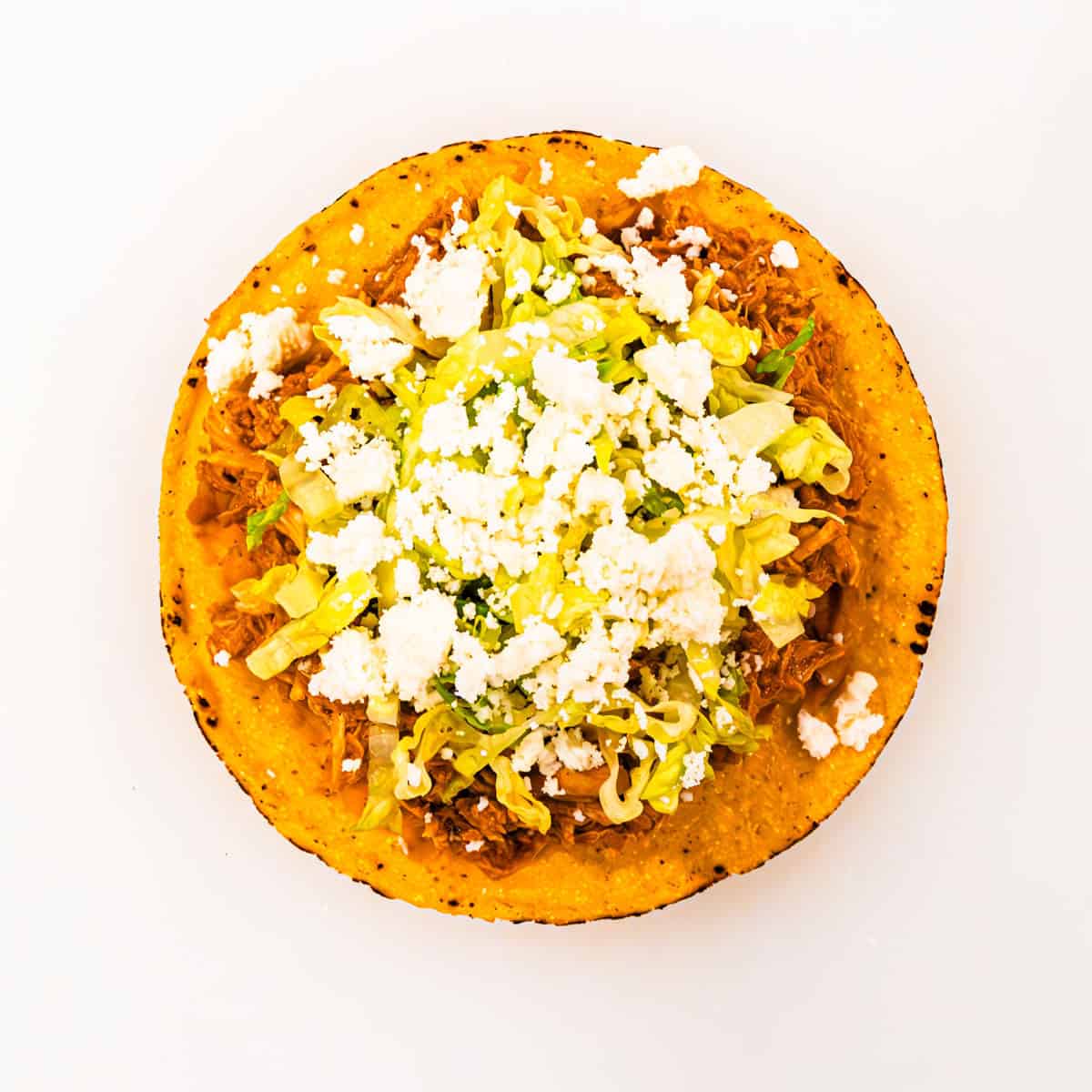Finished tostada topped with shredded lettuce and crumbled cheese.