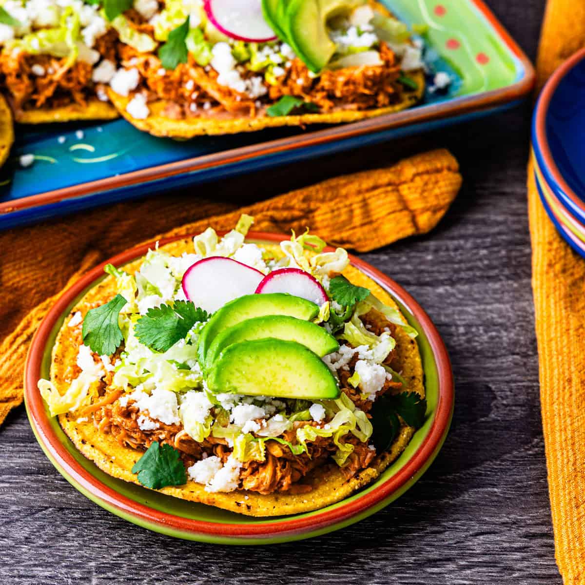 A chicken tinga tostada served on a plate next to a platter of tostadas.