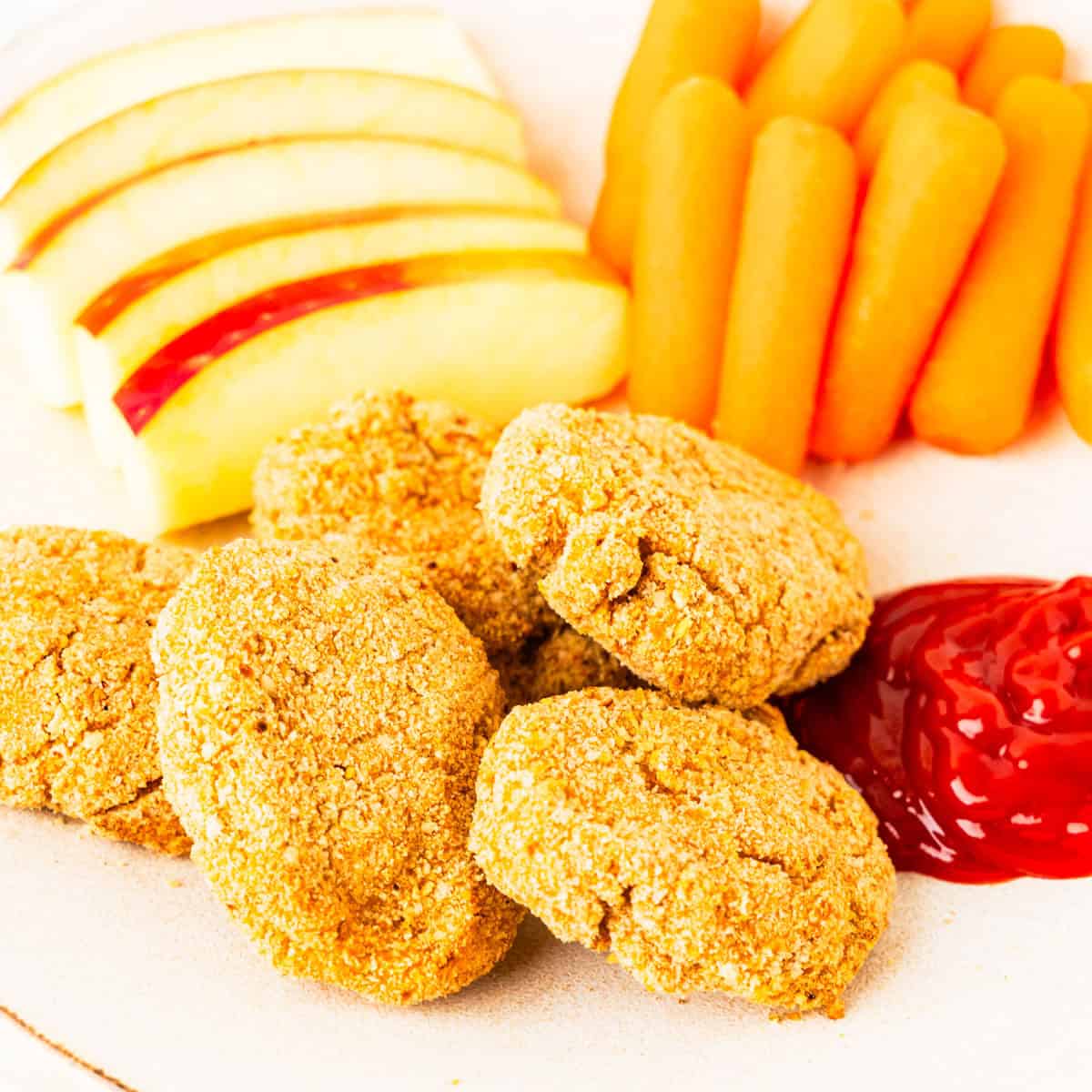 Chicken nuggets served with apples, carrots, and ketchup for dipping.